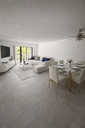 a living room with couches a coffee table a flat screen tv and a large window with kitchen view