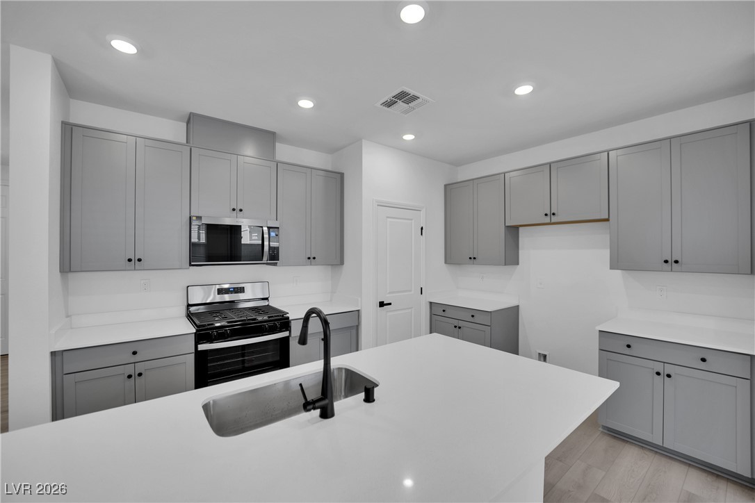 9136 Rivington Avenue Las Vegas, NV 89148 - Photo 6 of 43 Kitchen featuring gray cabinets, appliances with stainless steel finishes, recessed lighting, light wood finished floors, and light stone countertops