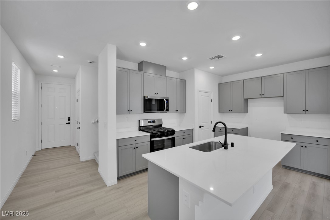 9136 Rivington Avenue Las Vegas, NV 89148 - Photo 8 of 43 Kitchen with gray cabinetry, appliances with stainless steel finishes, light wood-type flooring, a center island with sink, and recessed lighting