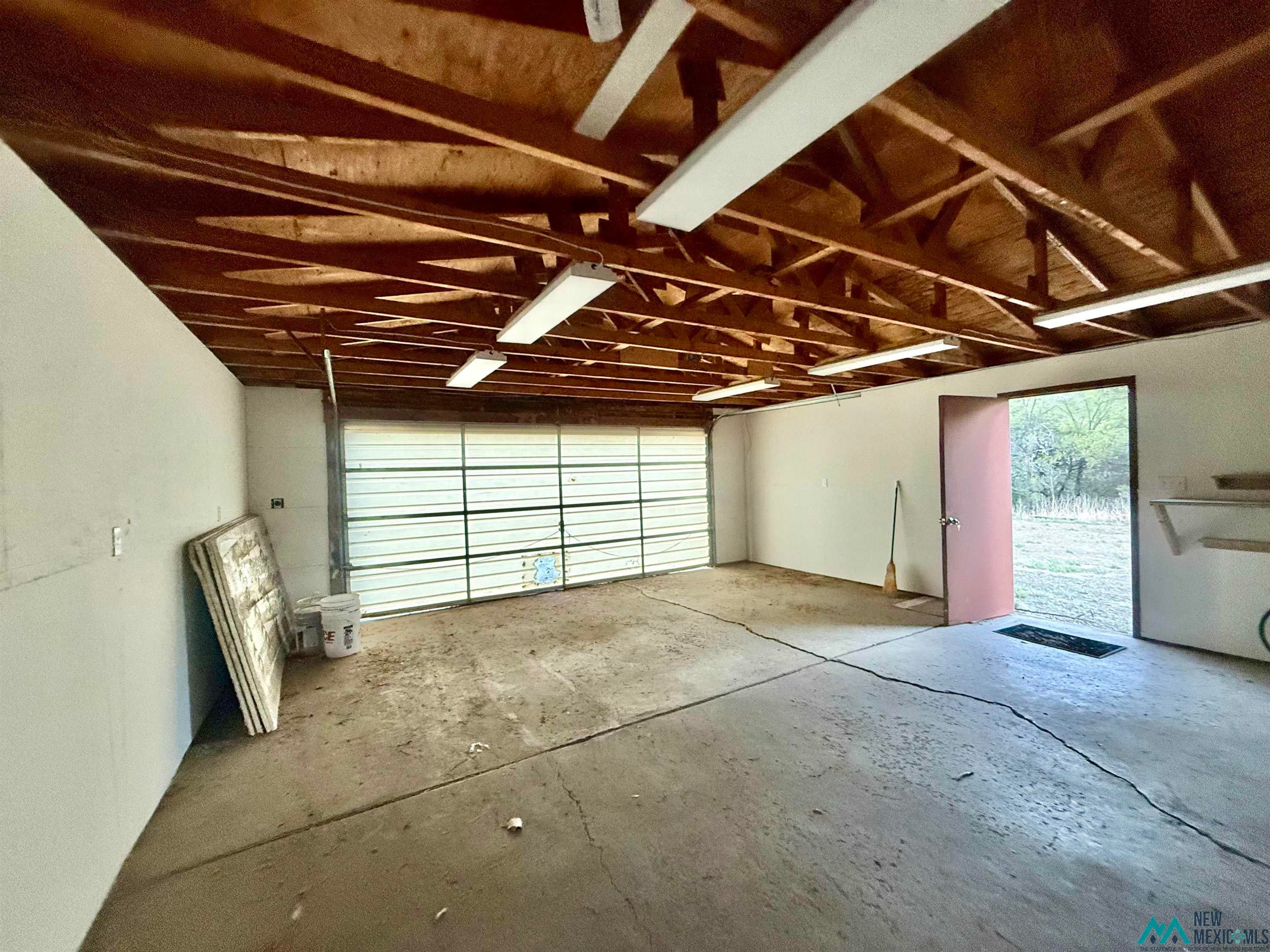 25 Linwood Road Raton, NM 87740 - Photo 4 of 41 Spacious garage featuring an overhead garage door, concrete flooring, exposed wood beam ceiling, and multiple fluorescent light fixtures