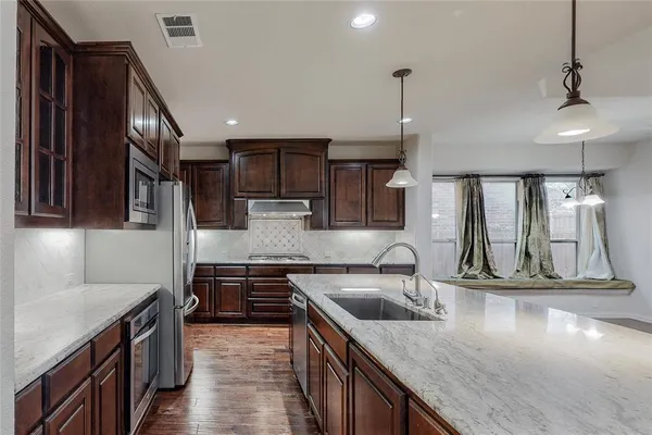 a kitchen with stainless steel appliances granite countertop a sink a stove and a wooden cabinets
