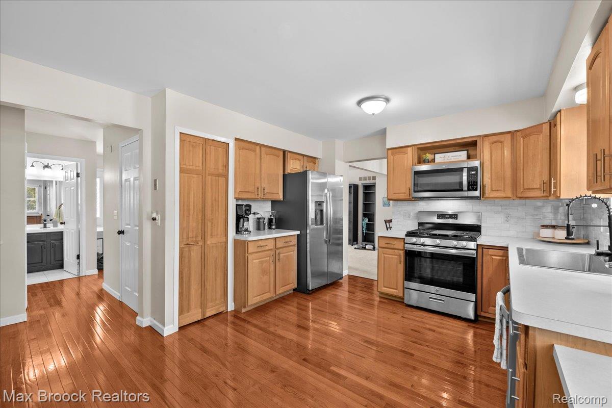 42470 Bishop Road Canton, MI 48188 - Photo 11 of 37 Spacious kitchen featuring wood cabinetry, stainless steel appliances including a French-door refrigerator and slide-in range, wood-finish flooring throughout, and ample counter space with a white apron-front sink