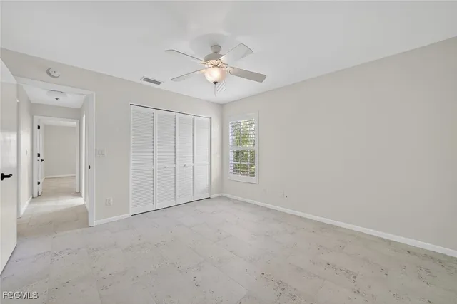 an empty room with chandelier fan and windows