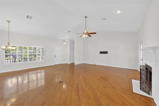 a view of an empty room with wooden floor a fireplace and a window