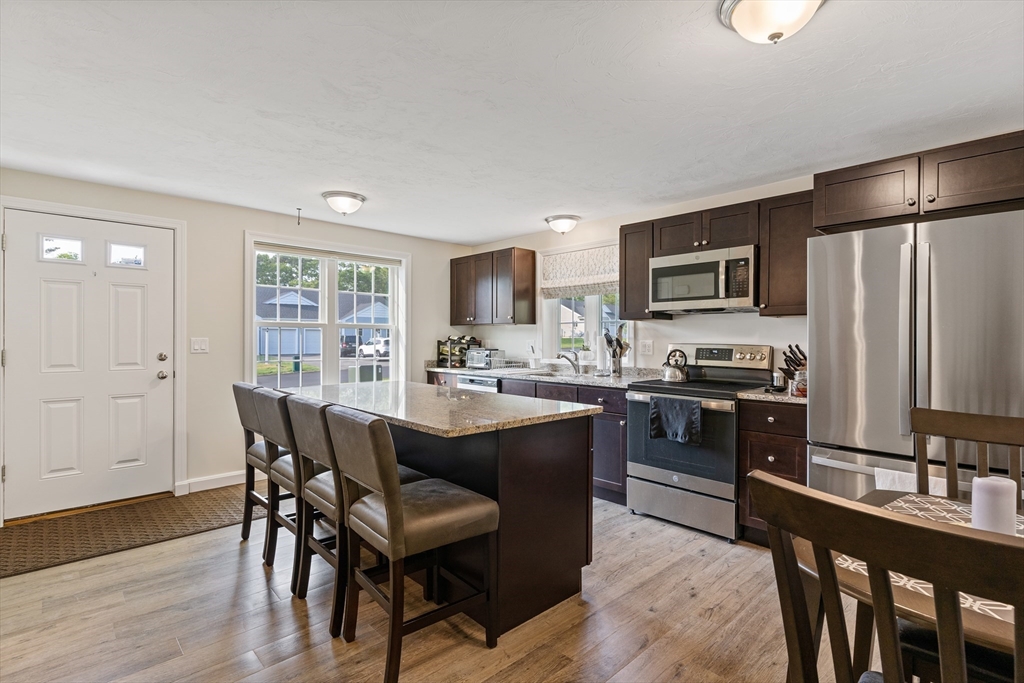 9 Tupper Hill Road, Unit 9 Plymouth, MA 02360 - Photo 10 of 30 a kitchen with stainless steel appliances granite countertop a stove a refrigerator a sink a dining table and chairs with wooden floor