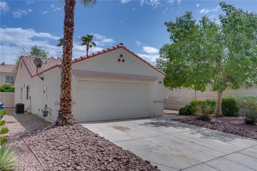 9660 Crystal Ridge Road Las Vegas, NV 89123 - Photo 2 of 13 Concrete driveway leads to a single garage, flanked by desert landscaping under a vibrant sky.