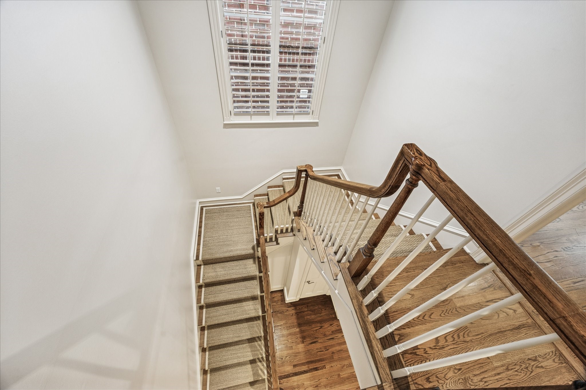 5823 Augusta Court Houston, TX 77057 - Photo 21 of 44 The home showcases a well-lit staircase with wooden railings and steps, seagrass carpeting as a runner. It features a large window with white shutters, enhancing the airy and open feel of the space.