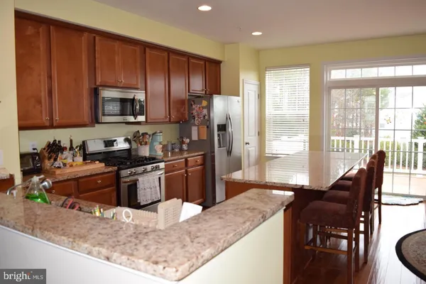 a kitchen with stainless steel appliances granite countertop a stove a sink a refrigerator a dining table and chairs