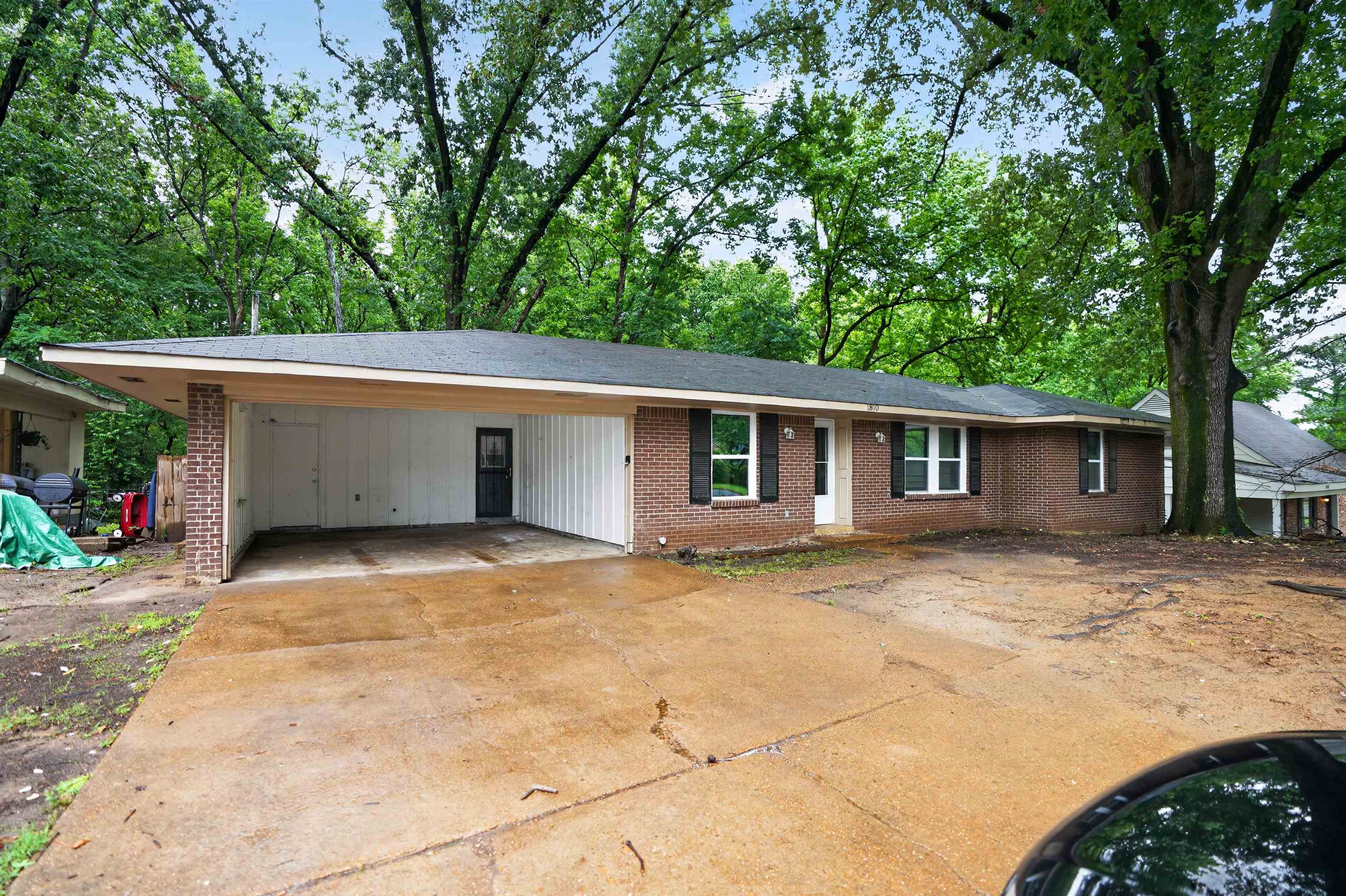 1890 Pennel Road Memphis, TN 38116 - Photo 2 of 25 Brick exterior featuring a covered carport, multi-pane windows with dark shutters, and mature trees providing natural canopy