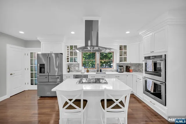 a kitchen with stainless steel appliances kitchen island granite countertop a refrigerator a stove a microwave oven a sink and white cabinets with wooden floor