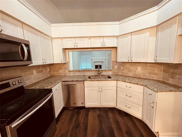 a kitchen with granite countertop white cabinets stainless steel appliances a sink and a window