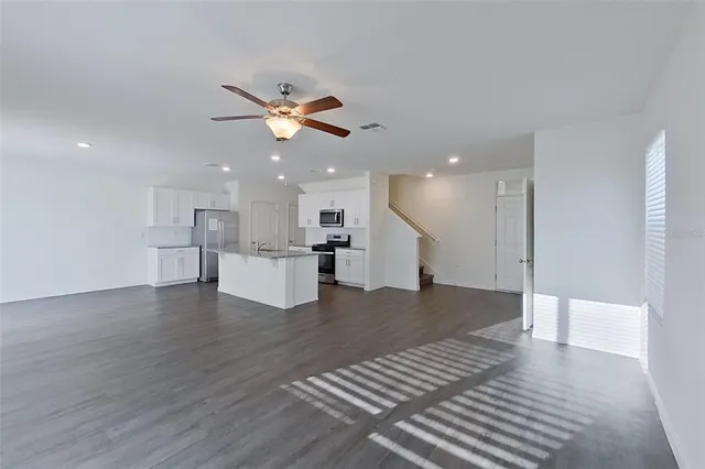 a view of an empty room with wooden floor and a kitchen