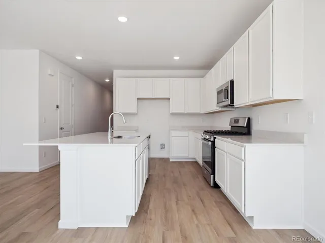 a kitchen with stainless steel appliances granite countertop a sink a stove a refrigerator and white cabinets with wooden floor