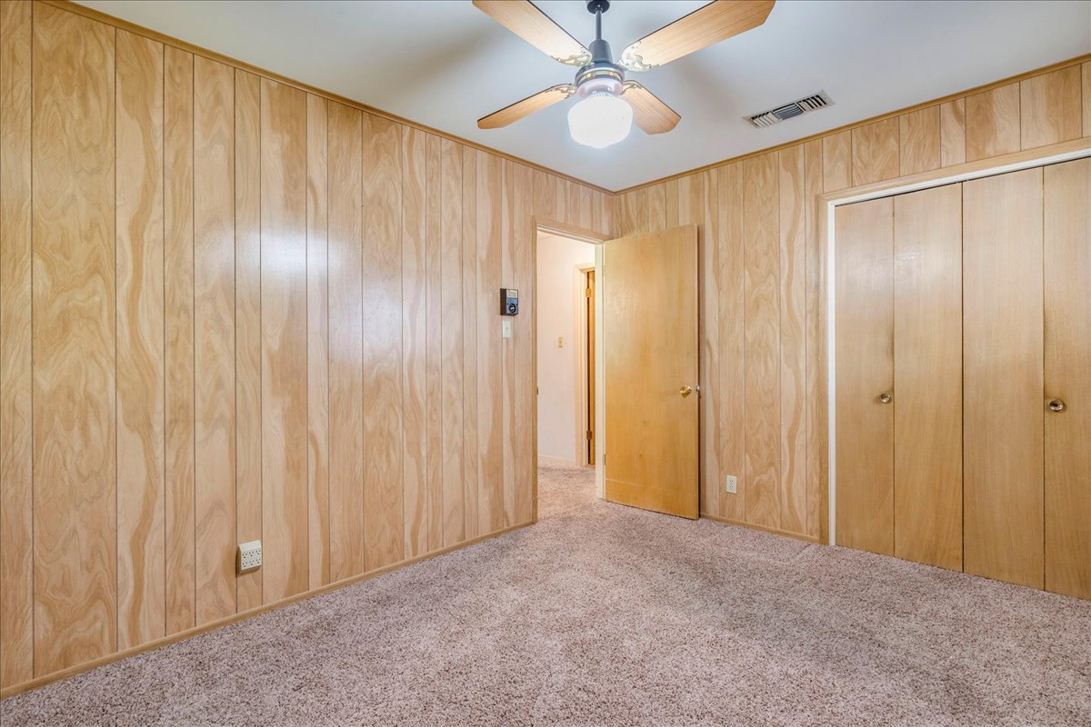 6626 Isabelle Drive Austin, TX 78752 - Photo 18 of 27 Bedroom featuring wood paneling, carpet flooring, a ceiling fan with light fixture, and two closet doors