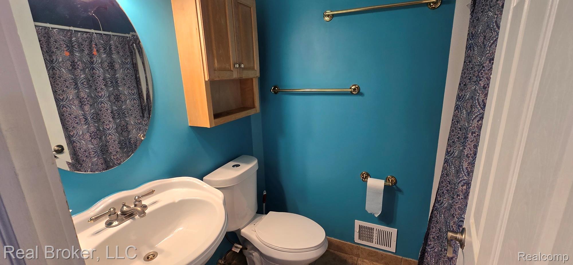 23401 Filmore Street Taylor, MI 48180 - Photo 13 of 16 Pedestal sink with polished chrome fixtures, round wall mirror, and natural wood cabinetry