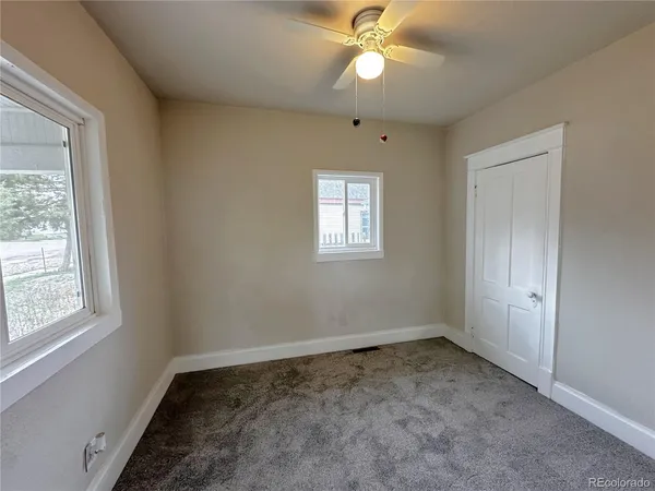an empty room with a chandelier fan and windows