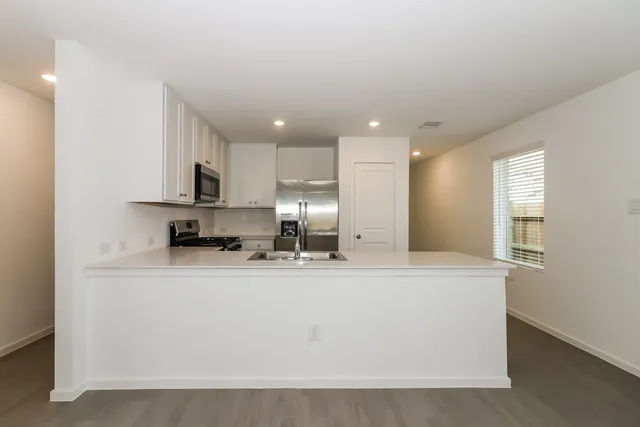 a large kitchen with stainless steel appliances granite countertop a stove a sink a refrigerator and white cabinets with wooden floor