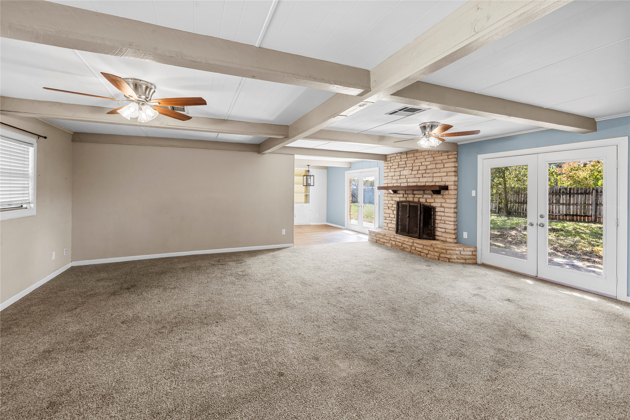 1401 Brazos Street Marble Falls, TX 78654 - Photo 5 of 23 Unfurnished living room with a ceiling fan, healthy amount of natural light, beam ceiling, a fireplace, and carpet flooring
