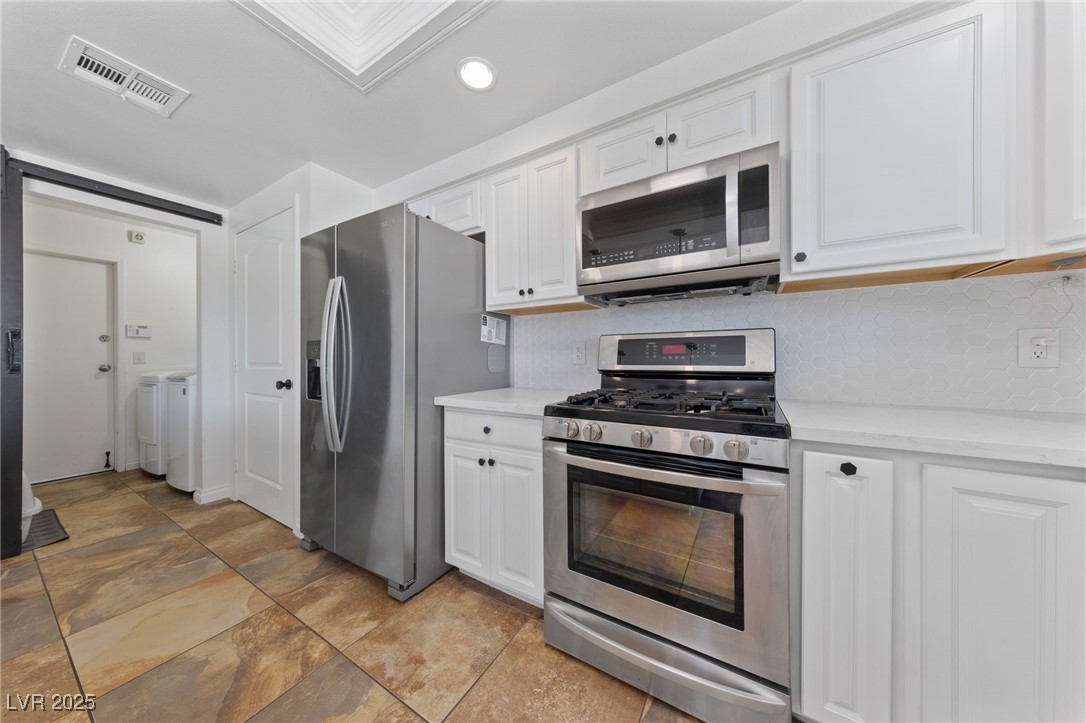 2637 Rialto Road Las Vegas, NV 89108 - Photo 6 of 22 Kitchen featuring stainless steel appliances, visible vents, decorative backsplash, washing machine and dryer, and white cabinets