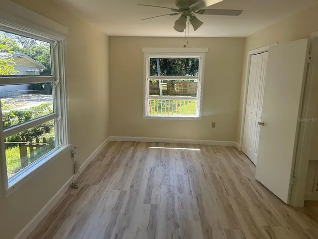 an empty room with wooden floor fan and windows