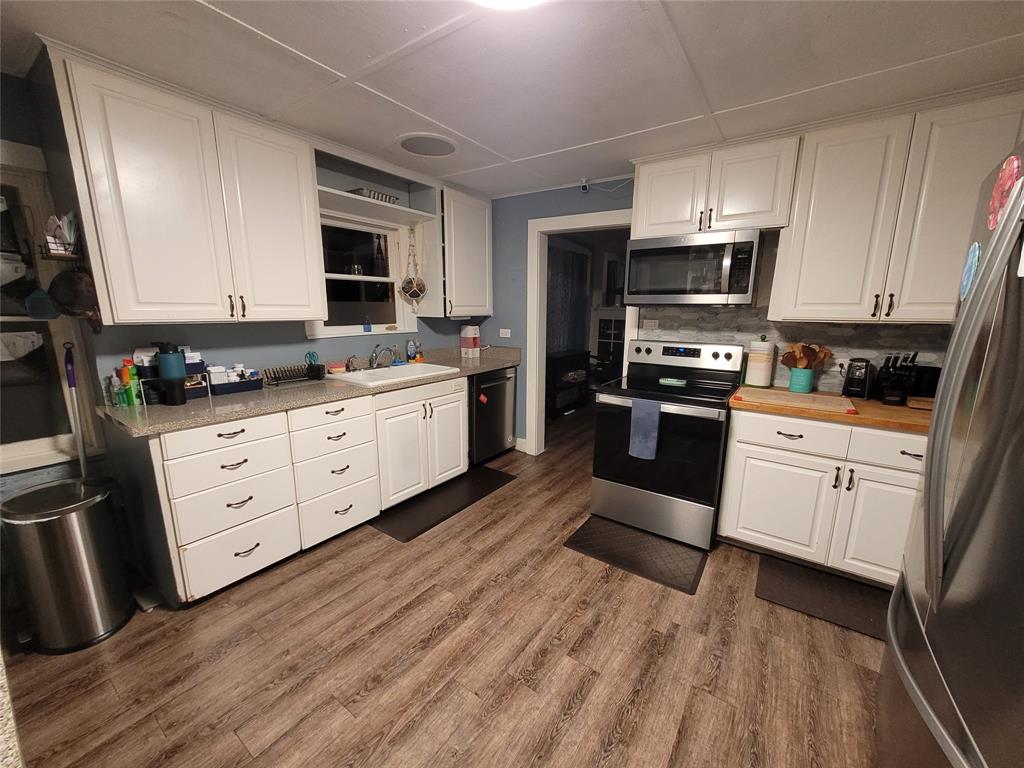 117 West 3rd Street, Unit A Keene, TX 76059 - Photo 7 of 14 a kitchen with stainless steel appliances granite countertop a stove top oven a sink dishwasher and white cabinets with wooden floor