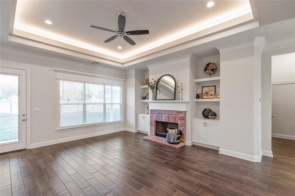331 Prien Lk Loop Bossier City, LA 71111 - Photo 7 of 37 Unfurnished living room with a tray ceiling, a ceiling fan, a fireplace, built in features, and dark wood-style flooring