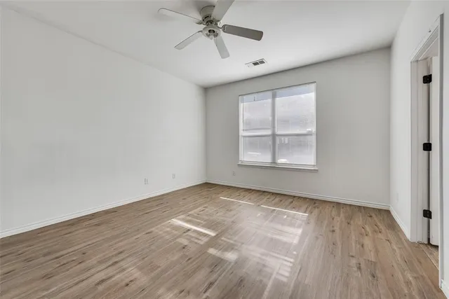 an empty room with wooden floor chandelier fan and windows