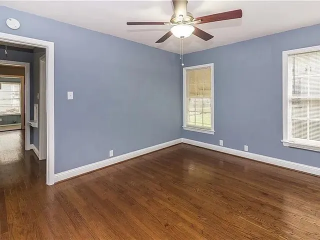 an empty room with wooden floor chandelier fan and windows