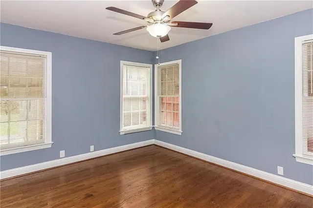 an empty room with wooden floor chandelier fan and windows