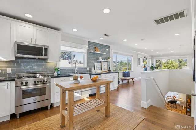 a kitchen with stainless steel appliances granite countertop a stove top oven a sink a dining table and chairs with wooden floor