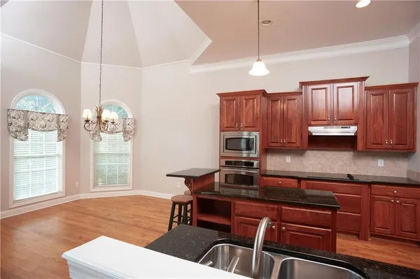 a kitchen with granite countertop a stove a sink dishwasher a dining table and chairs with wooden floor