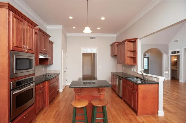 a kitchen with stainless steel appliances granite countertop a stove top oven a sink dishwasher and wooden cabinets with wooden floor