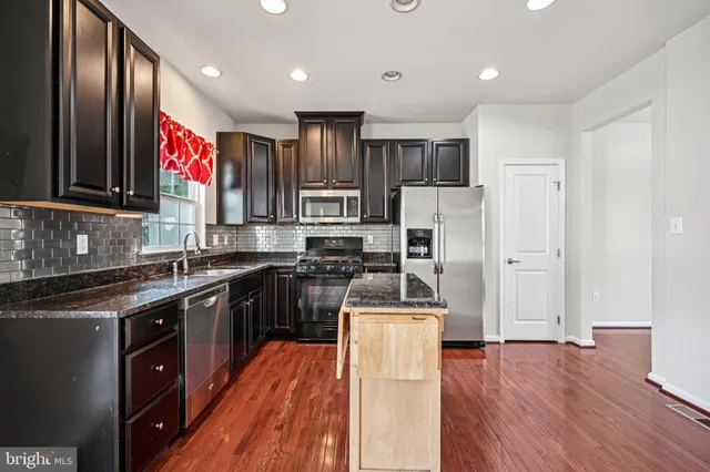 a kitchen with stainless steel appliances granite countertop a refrigerator a sink dishwasher a stove with wooden floor and cabinets