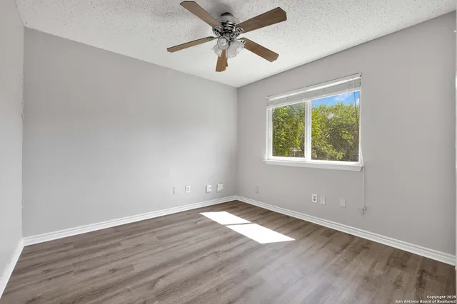 an empty room with wooden floor ceiling fan and windows