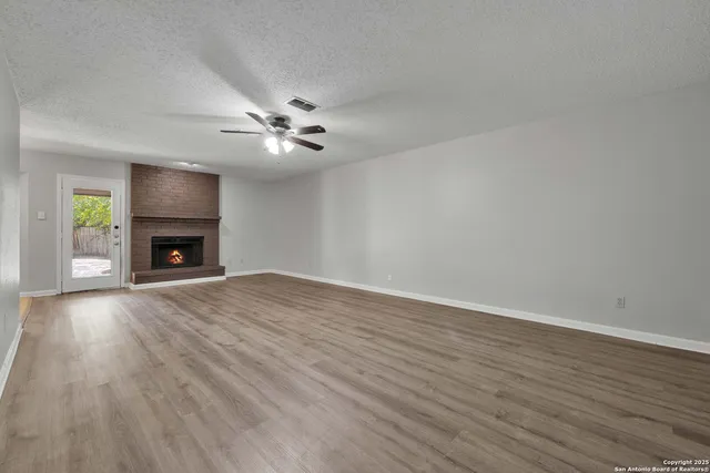 a view of an empty room with wooden floor fireplace and a window