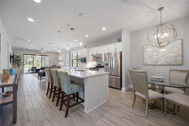 a kitchen with stainless steel appliances kitchen island granite countertop a dining table chairs refrigerator and microwave