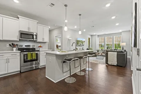 a open kitchen with stainless steel appliances granite countertop a stove top oven a sink dishwasher a dining table and chairs with wooden floor