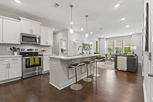 a open kitchen with stainless steel appliances granite countertop a stove top oven a sink dishwasher a dining table and chairs with wooden floor