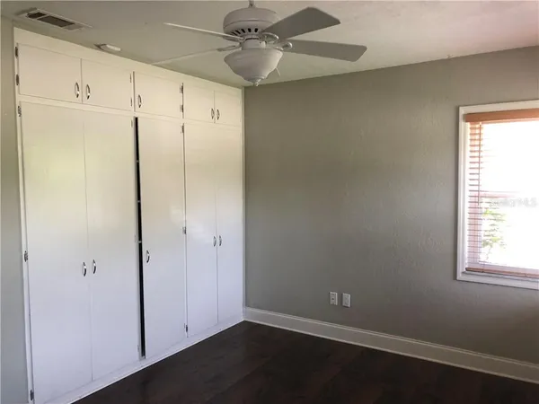 an empty room with wooden floor closet and windows