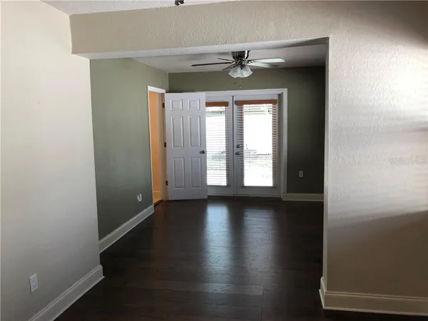 an empty room with wooden floor chandelier fan and windows