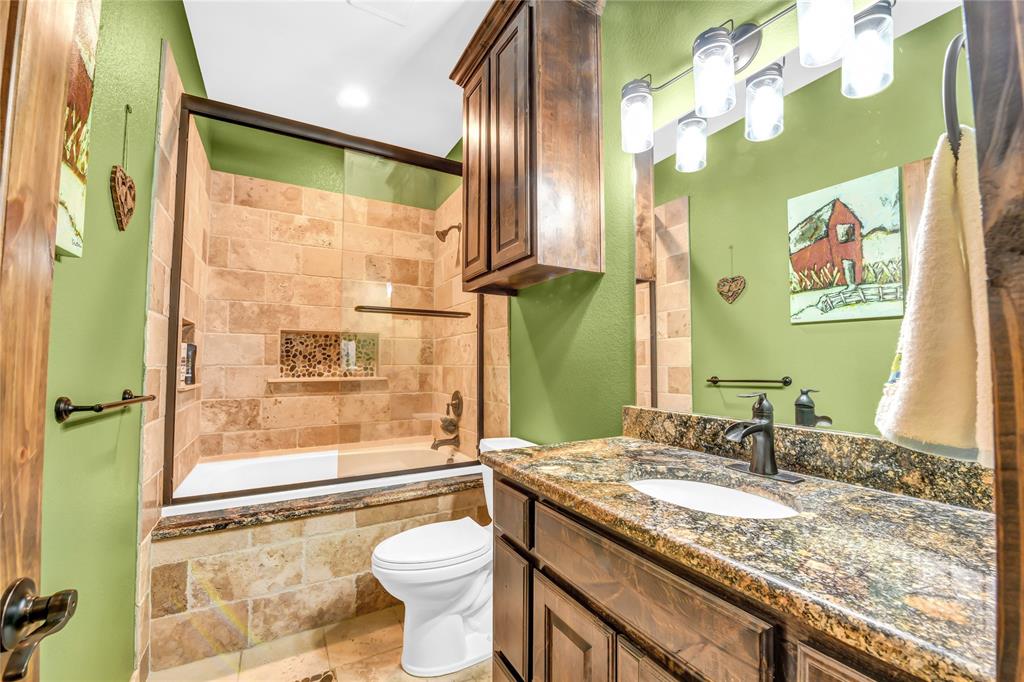 854 County Road 3330 Bridgeport, TX 76426 - Photo 23 of 40 Guest bath has a custom tiled shower / bath combo with a sitting ledge on the outside of the tub, tile patterned floor and granite countertop