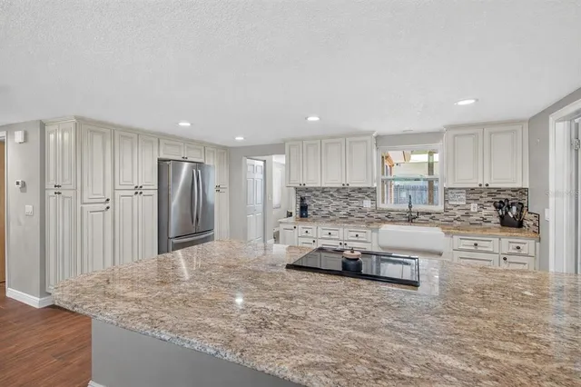 a large kitchen with kitchen island a stove a sink a refrigerator and white cabinets