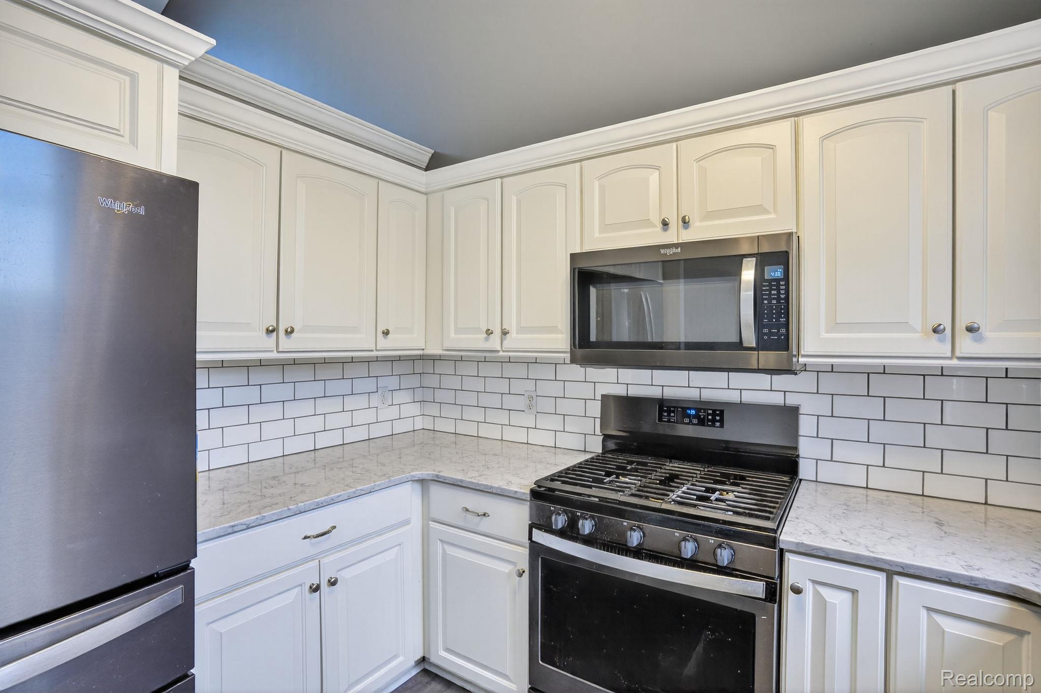 9055 Hegel Road Grand Blanc, MI 48439 - Photo 27 of 62 Kitchen featuring white shaker-style cabinetry with crown molding, stainless steel appliances, light-toned countertops, and a white subway tile backsplash