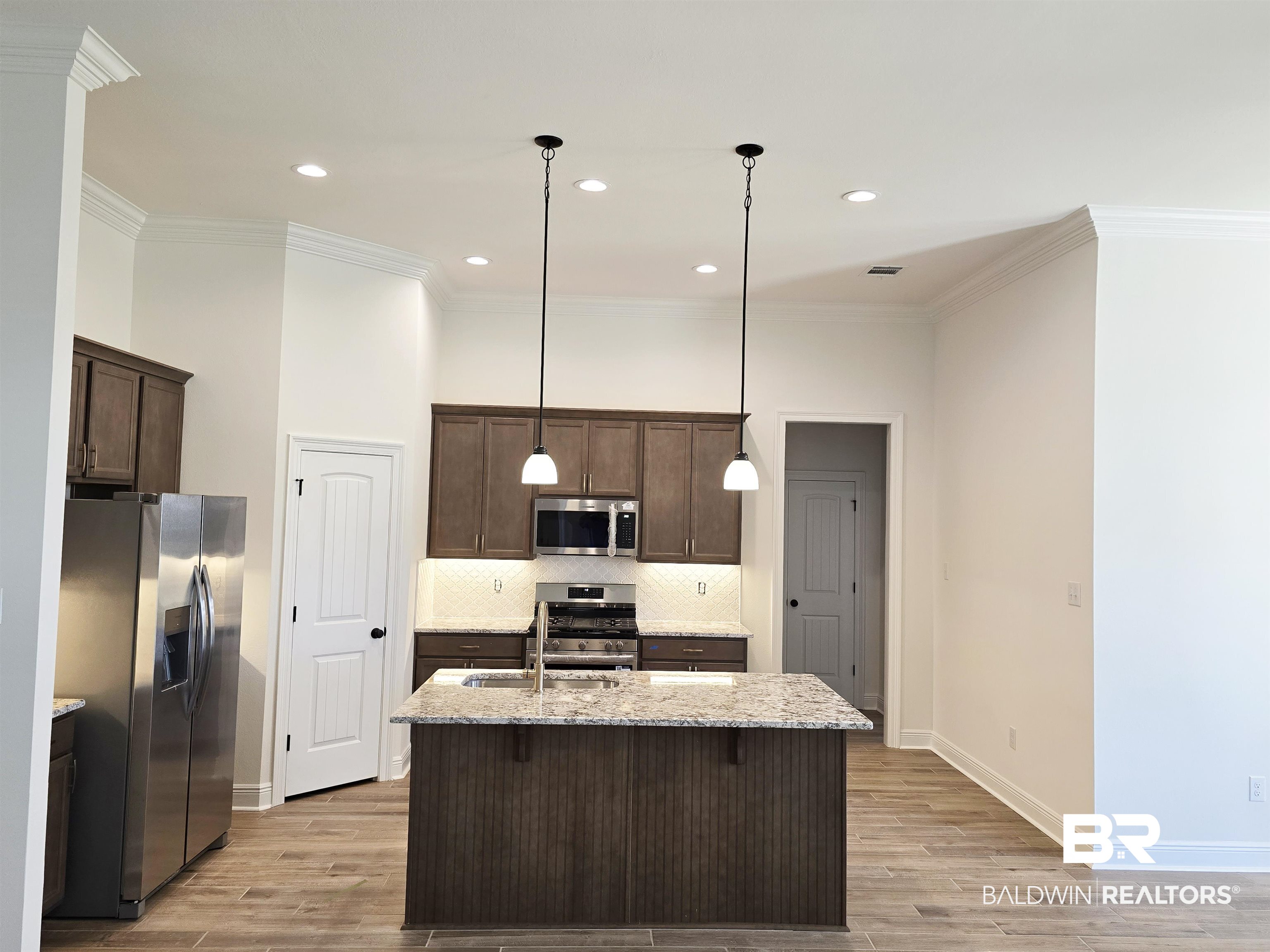 11178 Bonaventure Avenue Daphne, AL 36526 - Photo 2 of 20 Kitchen with light stone counters, crown molding, wood tiled floors, stainless steel appliances, and dark wood finish cabinetry