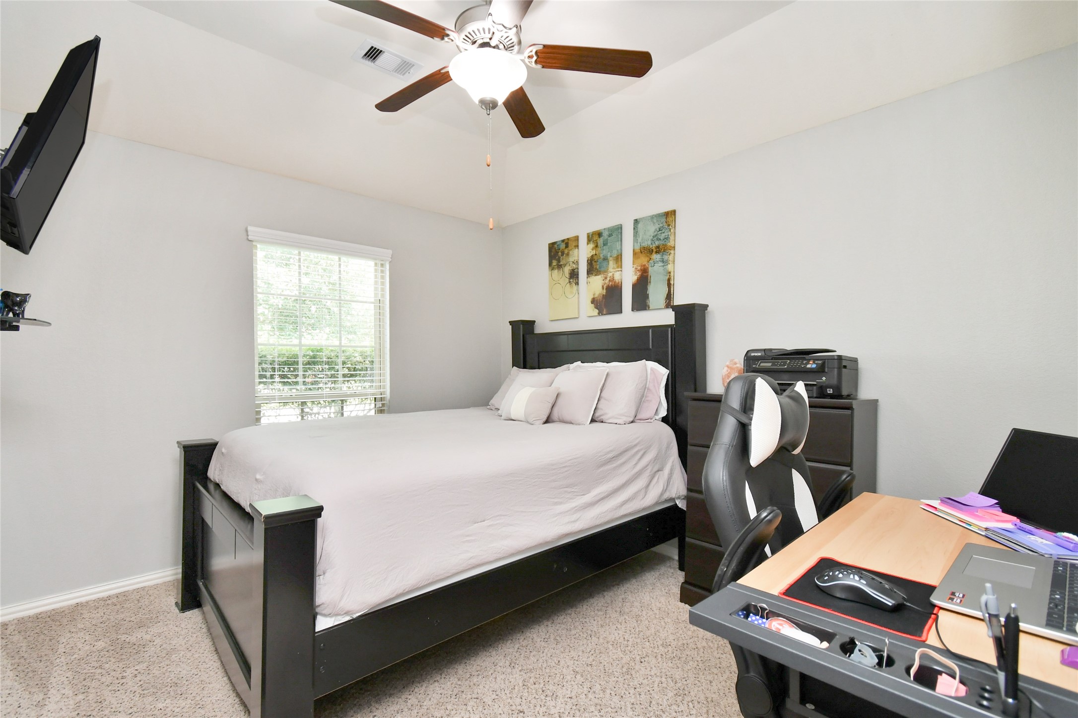 652 Maple Point Drive East Conroe, TX 77301 - Photo 17 of 35 This cozy bedroom features a large bed with a modern headboard, a ceiling fan, and a window providing natural light. A small desk with a chair and TV mounted on the wall add functionality. Neutral colors create a calm atmosphere.