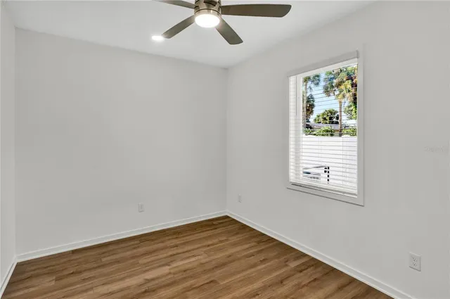 an empty room with wooden floor fan and windows