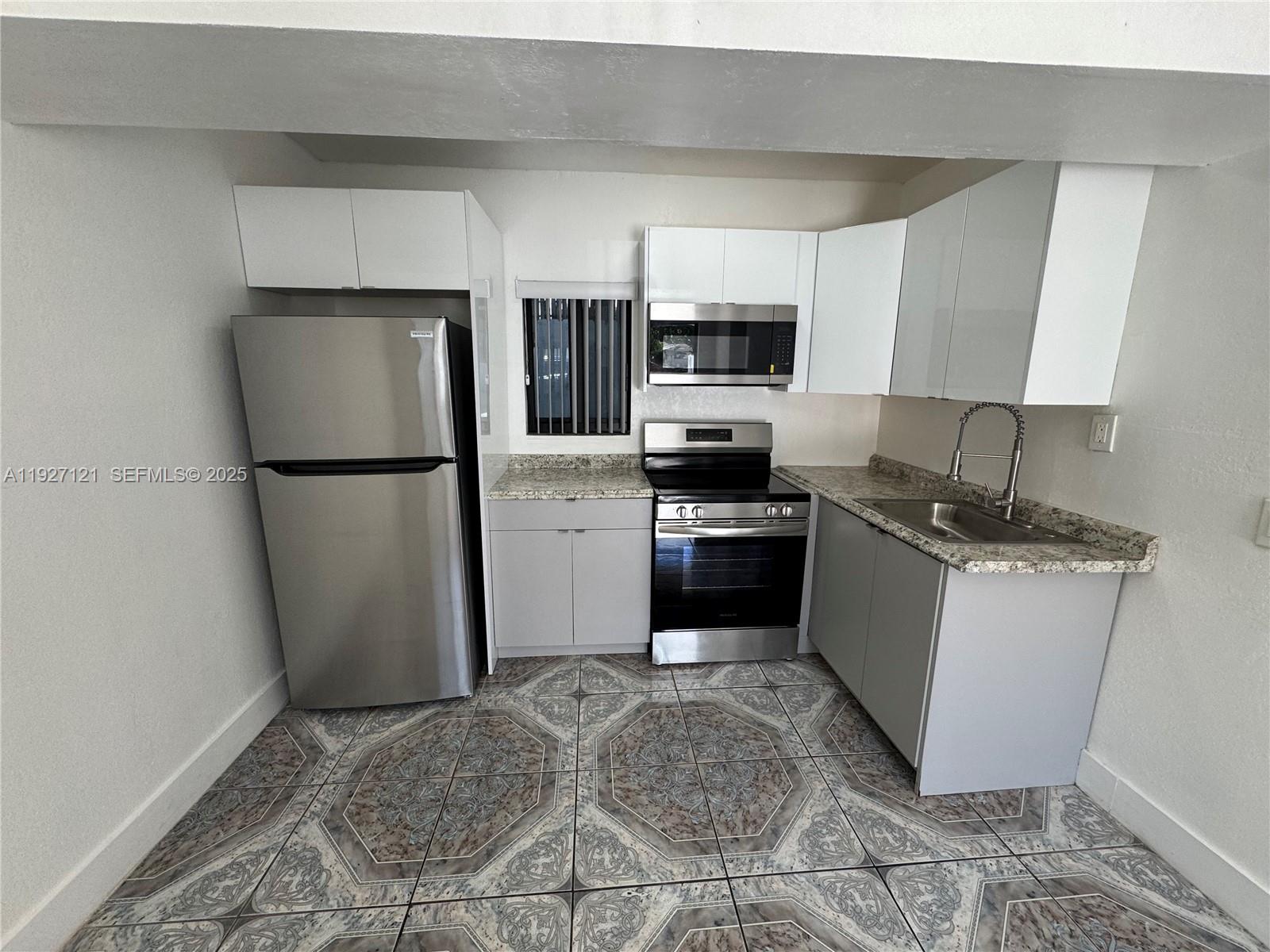 169 Northeast 50th Street, Unit 2 Miami, FL 33137 - Photo 3 of 16 a kitchen with a refrigerator a stove top oven and white cabinets