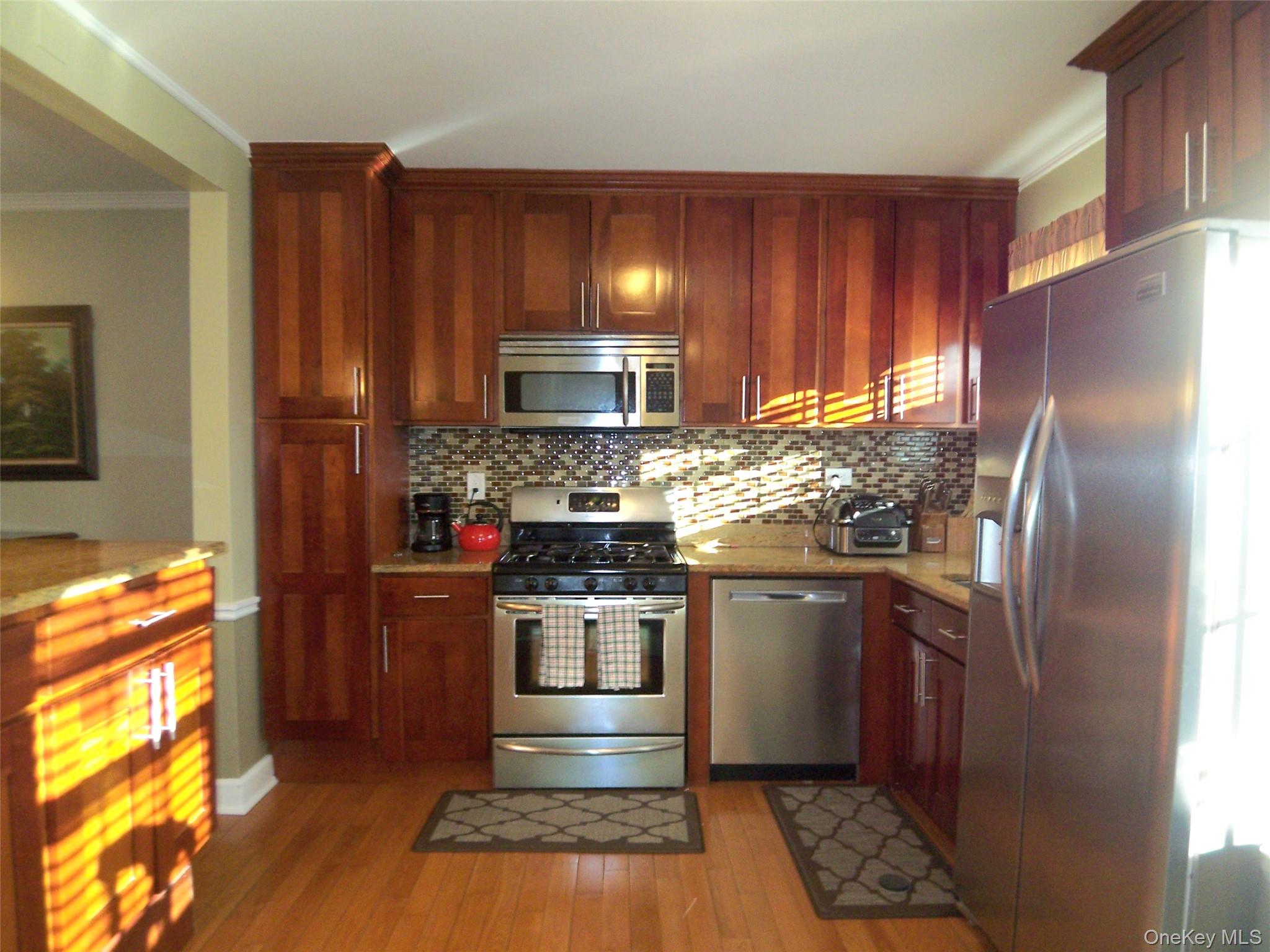 40 Harding Parkway Mount Vernon, NY 10552 - Photo 3 of 35 Kitchen featuring stainless steel appliances, crown molding, light wood-type flooring, light stone countertops, and decorative backsplash