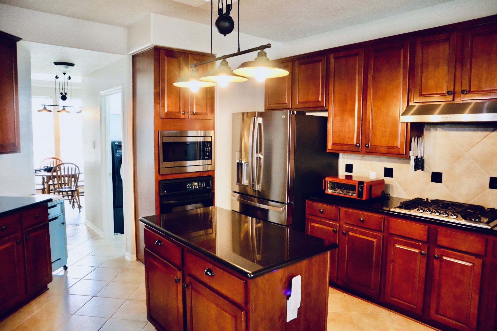 19114 Emory Trail Spring, TX 77388 - Photo 13 of 32 Chef's kitchen features rich wooden cabinetry, a central island with dark countertops, stainless steel appliances, and a gas stove. It opens to a dining area with natural light.