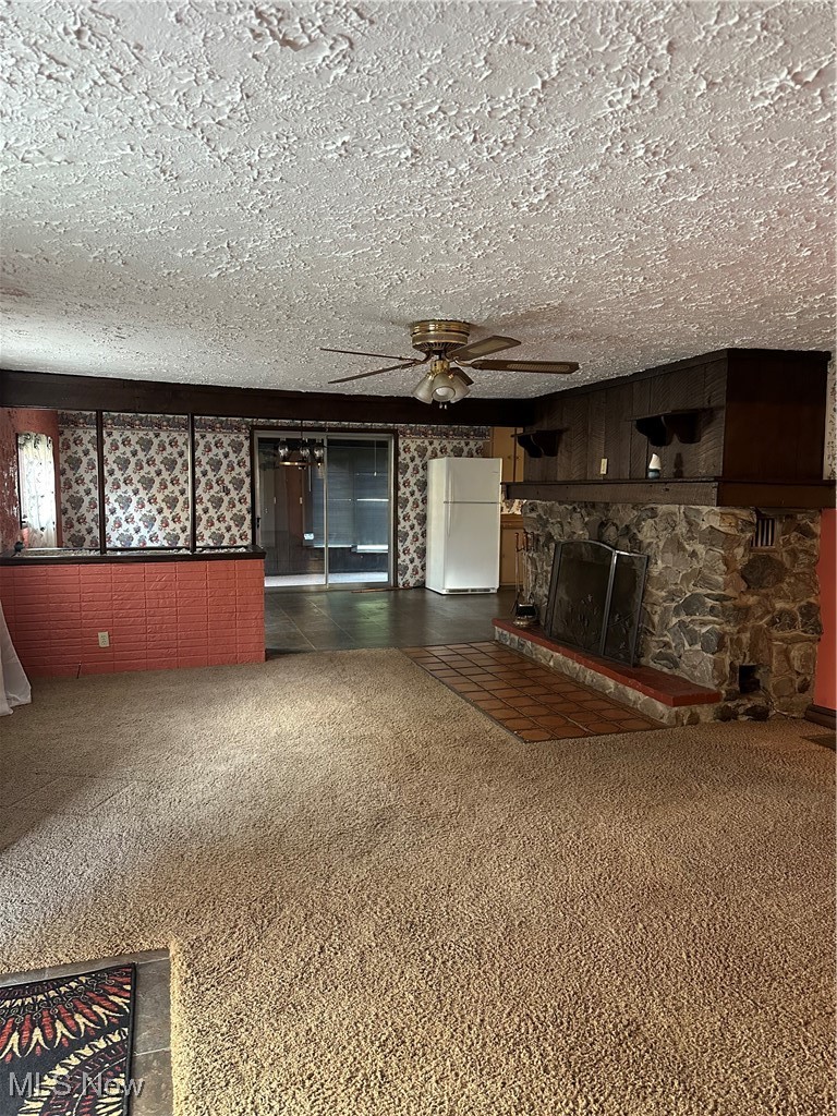 44952 Moose Ridge Road Woodsfield, OH 43793 - Photo 14 of 48 Living room featuring carpet flooring, a stone fireplace, a ceiling fan, and a textured ceiling